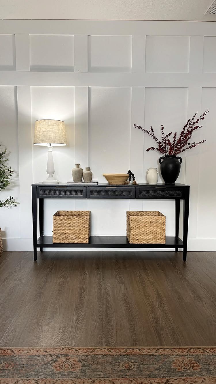 White paneled wainscoting accent wall behind a black console table with decor.