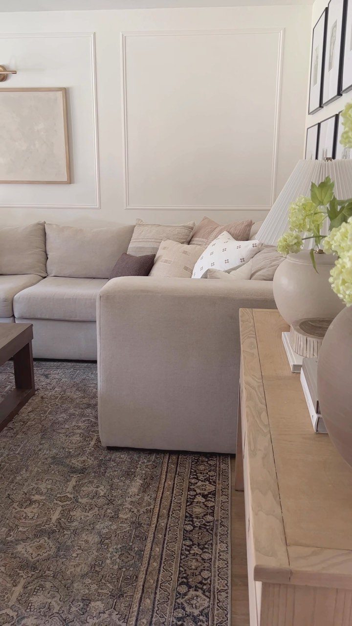 Grey sectional sofa positioned against a white wall with decorative picture frame wainscoting molding.