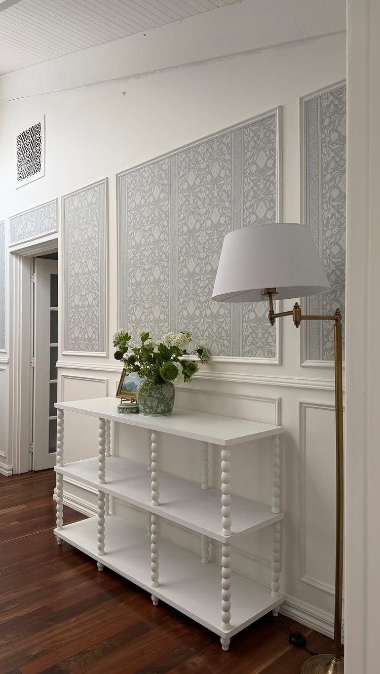 White wainscoting panels on a wall behind a white console table and a floor lamp.