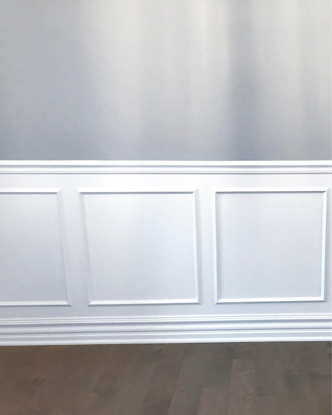 White decorative wainscoting panels installed on a wall above dark wood flooring.