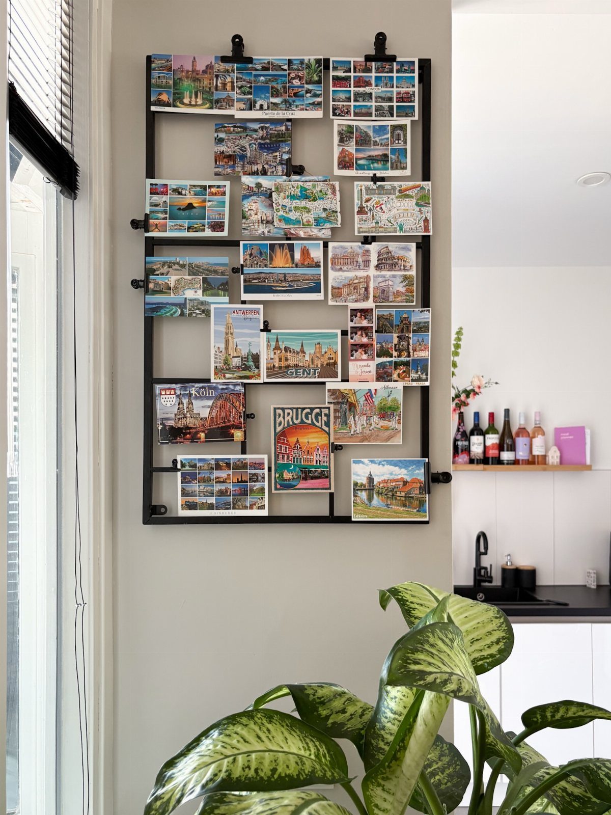 23 Wall Decor Design Ideas (Gallery Walls, Moss Walls, Rattan) 18 A black metal grid frame displaying numerous colorful travel postcards clipped to the wires on a wall.