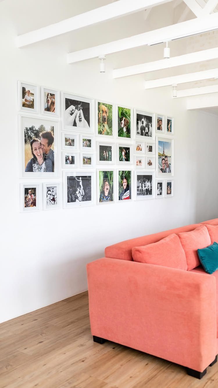 23 Wall Decor Design Ideas (Gallery Walls, Moss Walls, Rattan) 10 White framed photographs arranged in a gallery wall pattern on a white wall above a coral sofa.