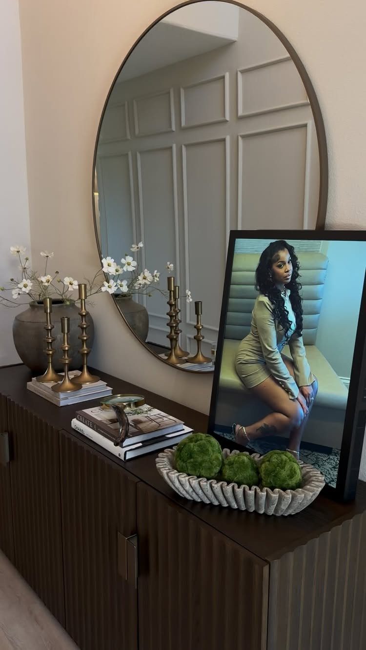 23 Wall Decor Design Ideas (Gallery Walls, Moss Walls, Rattan) 3 Oval mirror hanging above a dark wooden sideboard with decor and a framed portrait.