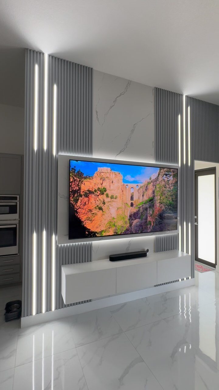 23 Wall Decor Design Ideas (Gallery Walls, Moss Walls, Rattan) 19 Modern feature wall with vertical slats, LED lighting, marble panel, and a large television.