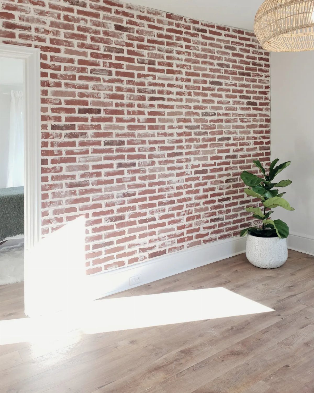 23 Wall Decor Design Ideas (Gallery Walls, Moss Walls, Rattan) 14 Red brick patterned accent wall in a bright room with light wood floors and a potted plant.