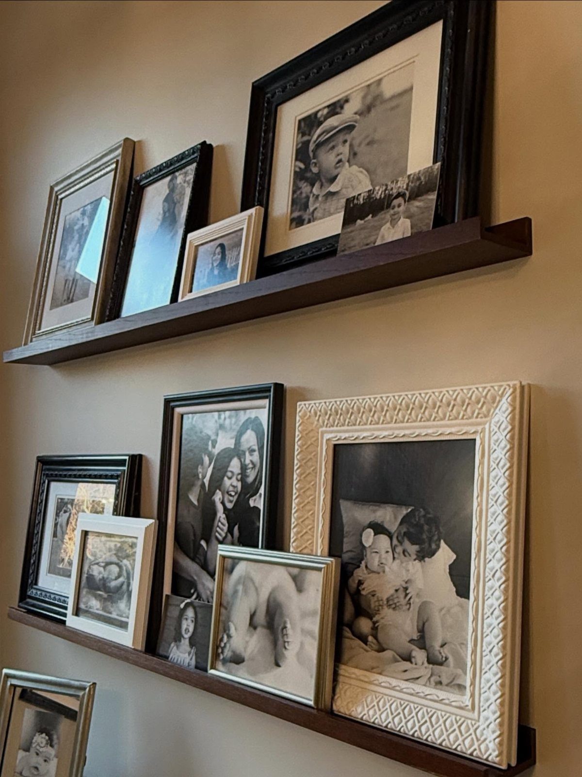 23 Wall Decor Design Ideas (Gallery Walls, Moss Walls, Rattan) 15 Two dark wood floating shelves displaying various framed black and white family photographs on a beige wall.