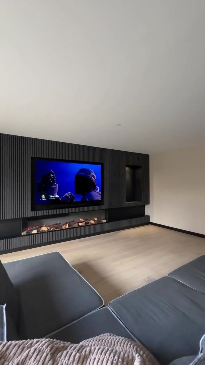 Dark vertically slatted wall panels featuring a built-in television and a modern fireplace in a living room.
