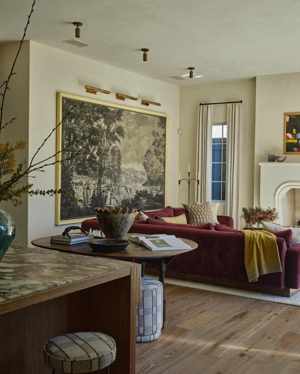 Large gold-framed landscape wallpaper hanging on a cream wall above a red sofa.
