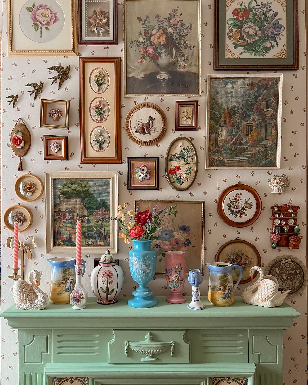 Framed botanical art and decorative plates arranged on a patterned wallpaper accent wall above a green sideboard.