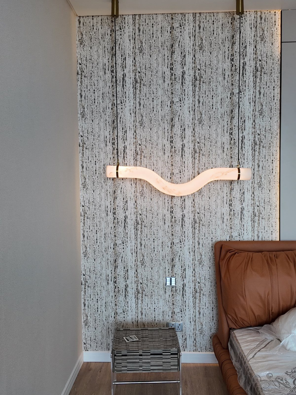 Textured grey and white patterned wallpaper on a wall with a wavy pendant light.