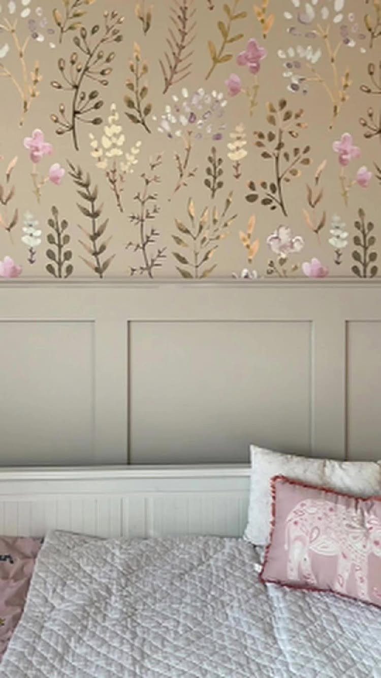 Floral patterned wallpaper above grey wainscoting in a bedroom with a white bed.