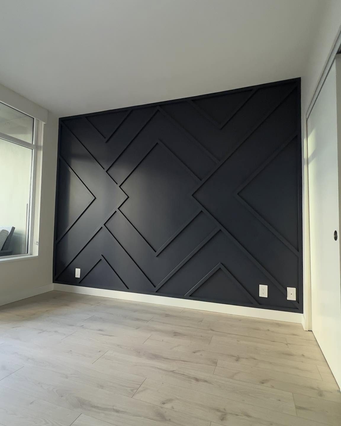 Black geometric wood slat accent wall in a bright room with light wood floors.