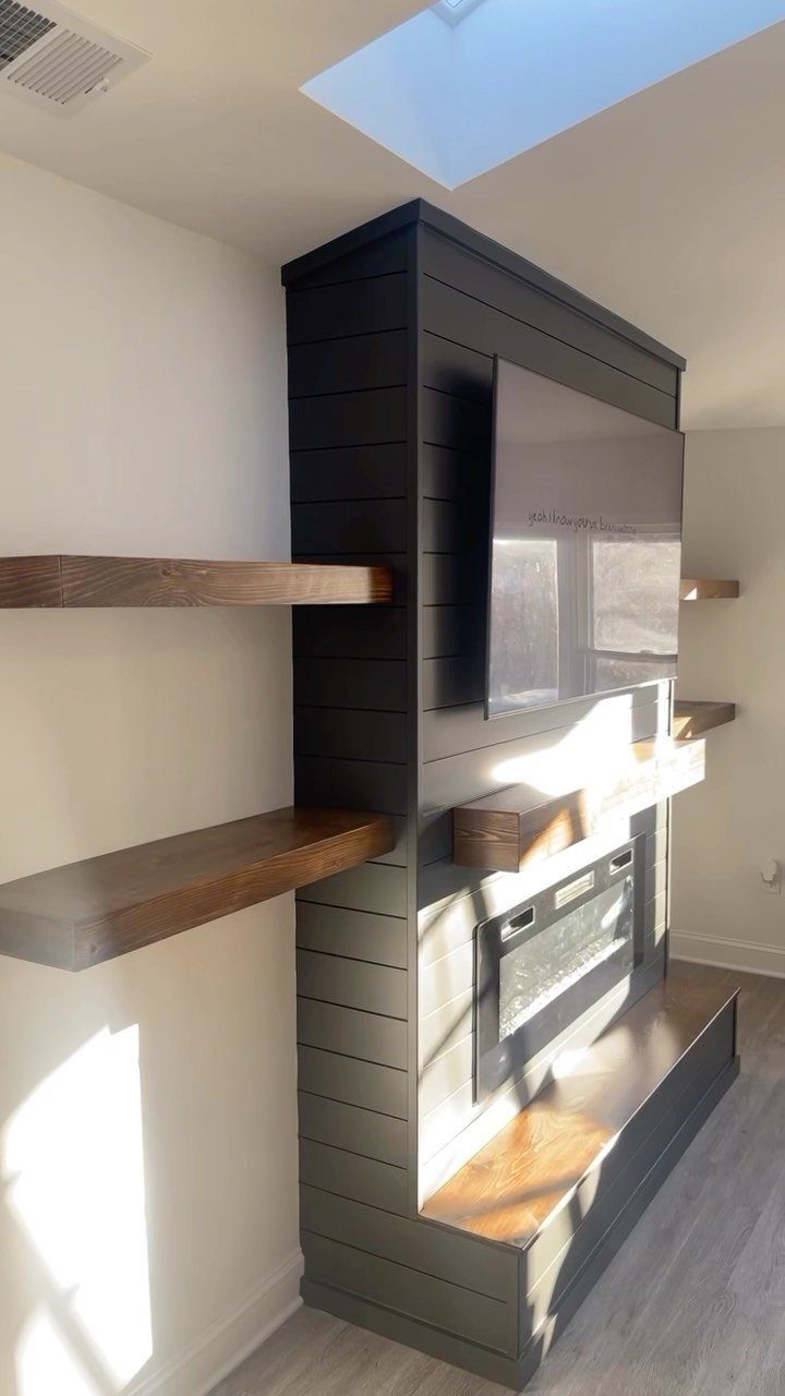 Dark grey shiplap accent wall with a fireplace, television, and wooden floating shelves.
