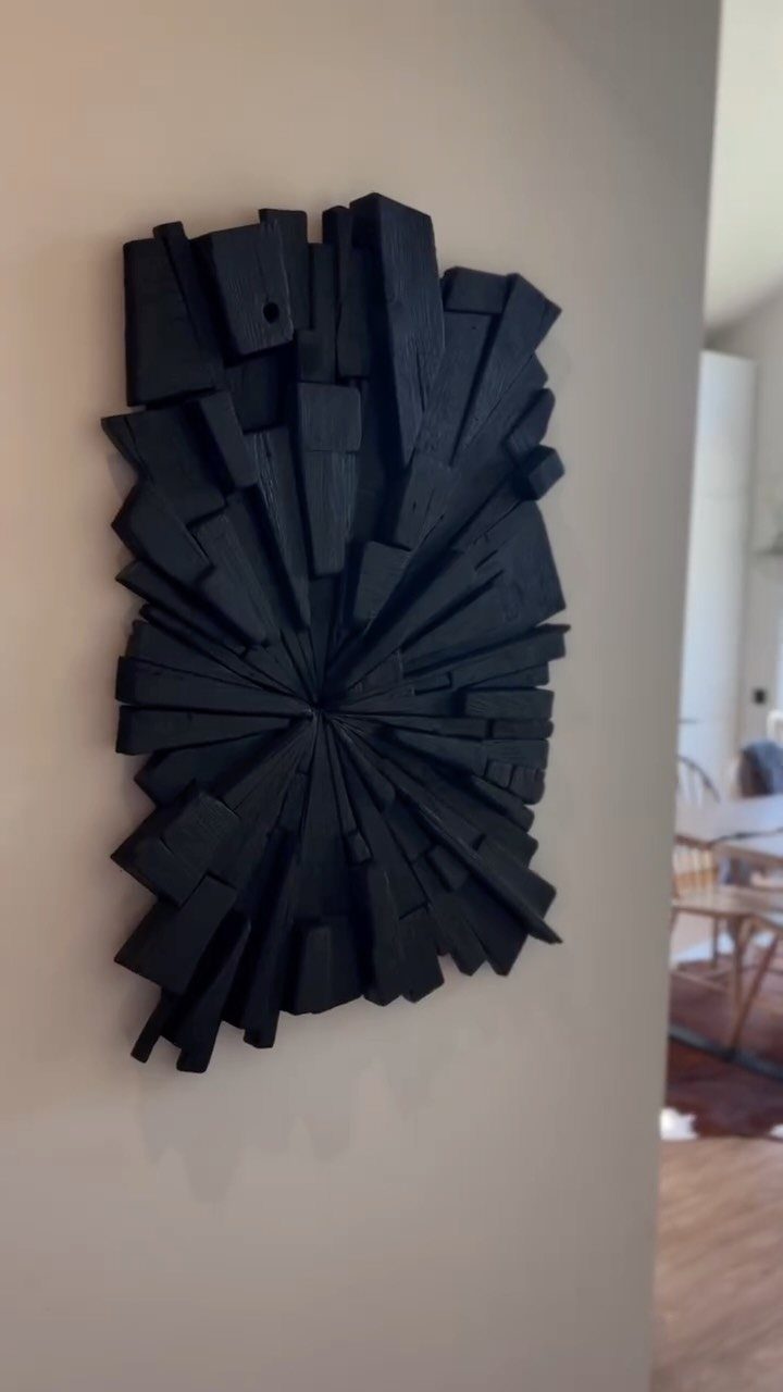 Black wooden block sculpture radiating from a center point mounted on a plain light wall.