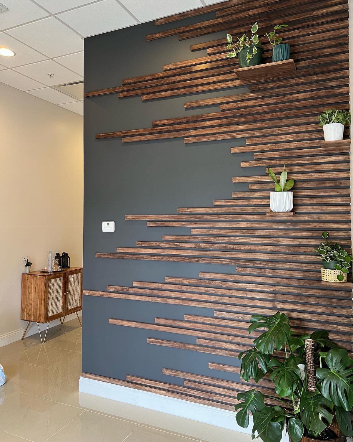 Horizontal dark wood slats arranged in a geometric pattern on a dark gray accent wall with plants.