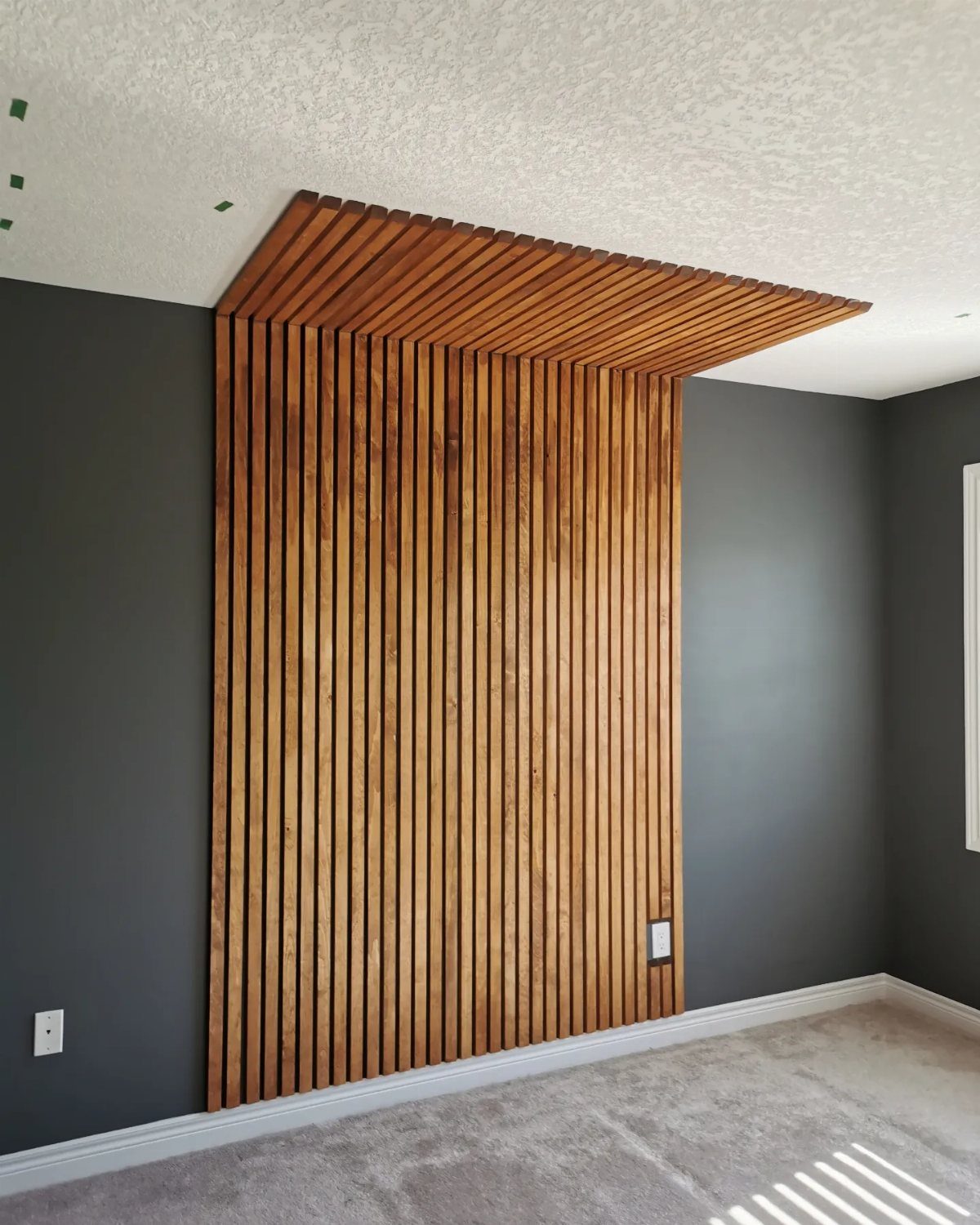 Vertical wooden slats covering a dark grey wall and extending onto the ceiling in a room.