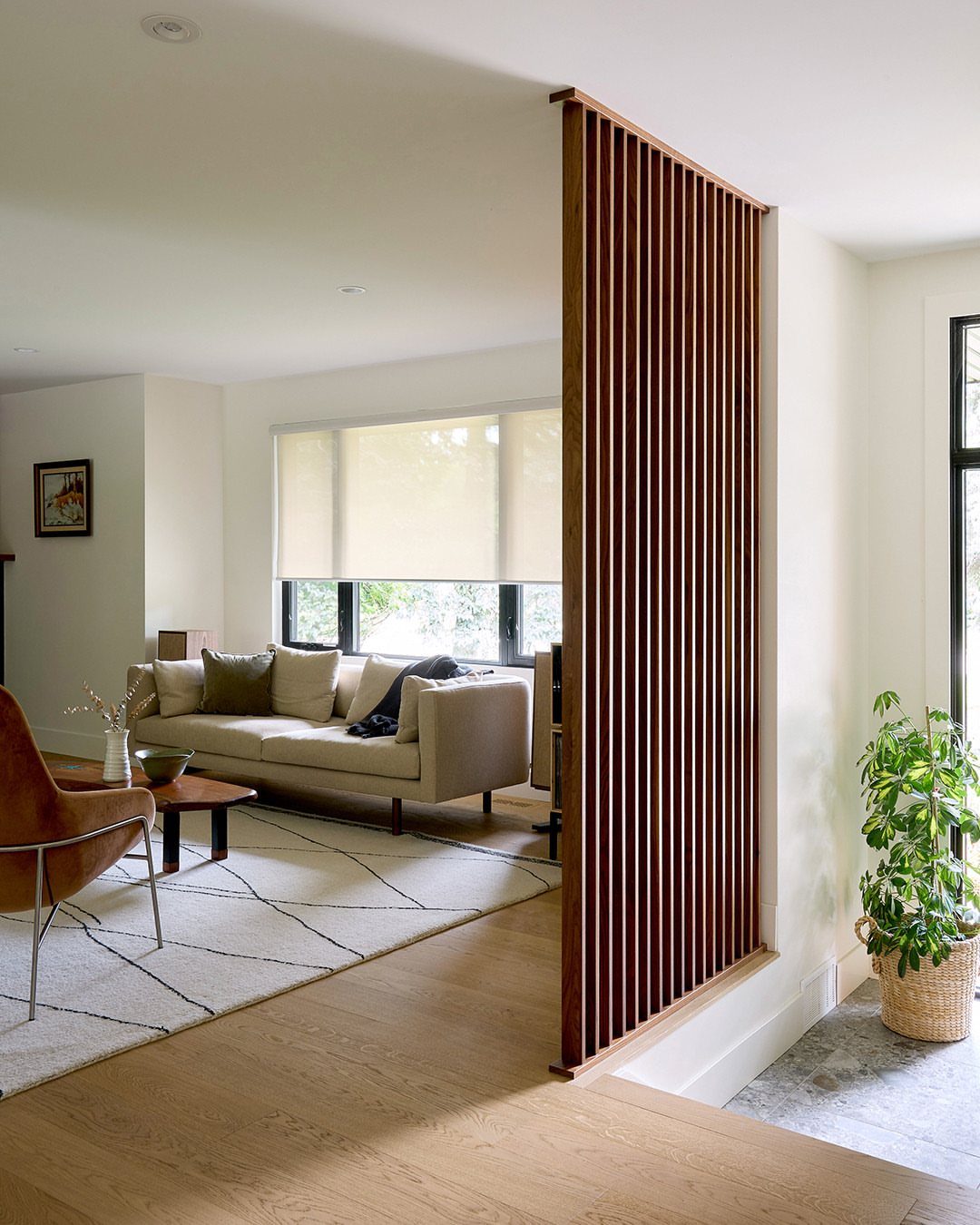 Vertical wood slat room divider separating a modern living room from a hallway.