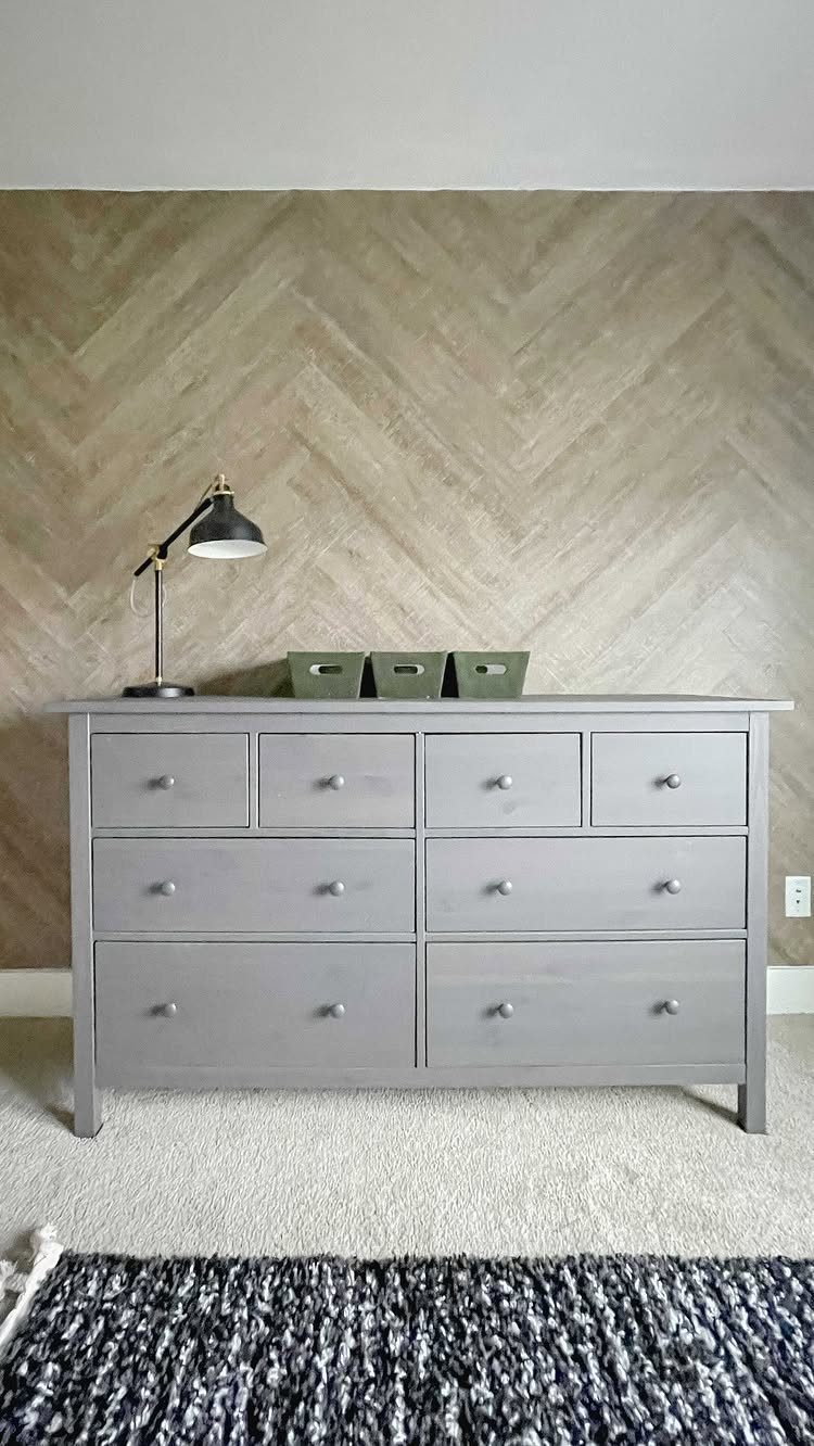 Wooden Plank Design: 6 Looks for Walls and Accents 5 Light brown wooden planks arranged in a chevron pattern on a wall behind a grey dresser.